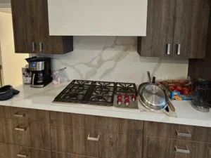 Modern kitchen with wood-grain flat-panel cabinets, white veined quartz backsplash, and built-in gas cooktop