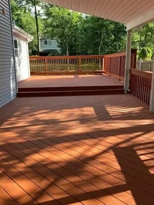 Reddish-brown stained deck boards and railings with white covered porch posts and gray siding