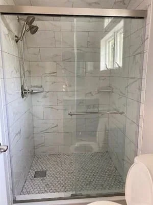 Walk-in shower with marble-look wall tile, hexagonal mosaic floor, brushed metal glass sliding door, and grab bar