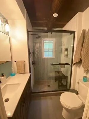 Small bathroom with glass sliding shower door, gray tile, dark wood-look ceiling, and white vanity with undermount sink