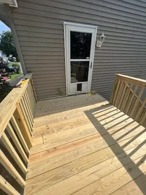 New pressure-treated wood deck with lumber railing beside gray vinyl siding and white storm door