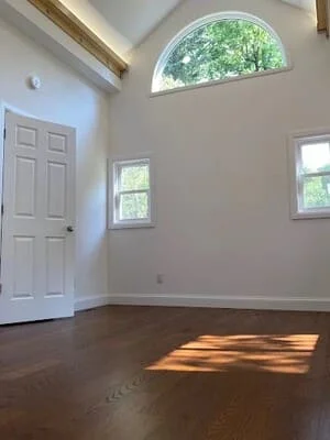 Freshly painted white walls and trim in a vaulted room with exposed beams, arched window, and dark hardwood floors