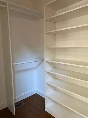 White painted closet with built-in shelving and hanging rod over dark hardwood floor