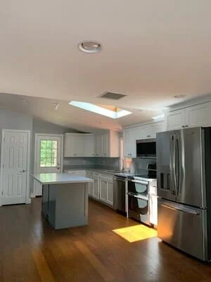 Kitchen with white painted cabinets, gray painted island, vaulted ceiling, skylight, and stainless steel appliances over wood flooring