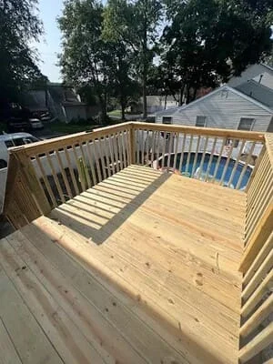 New pressure-treated wood deck with vertical baluster railing and stairs beside an above-ground pool