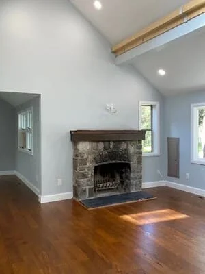 Vaulted living room with light gray painted walls, white trim, stone fireplace with wood mantel, and hardwood floors