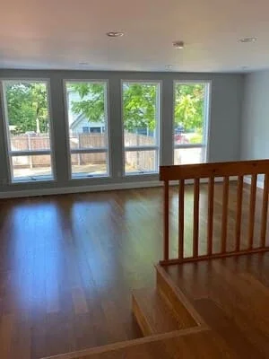 Interior living room with four tall white-framed windows, gray painted walls, hardwood floors, and a wood staircase railing